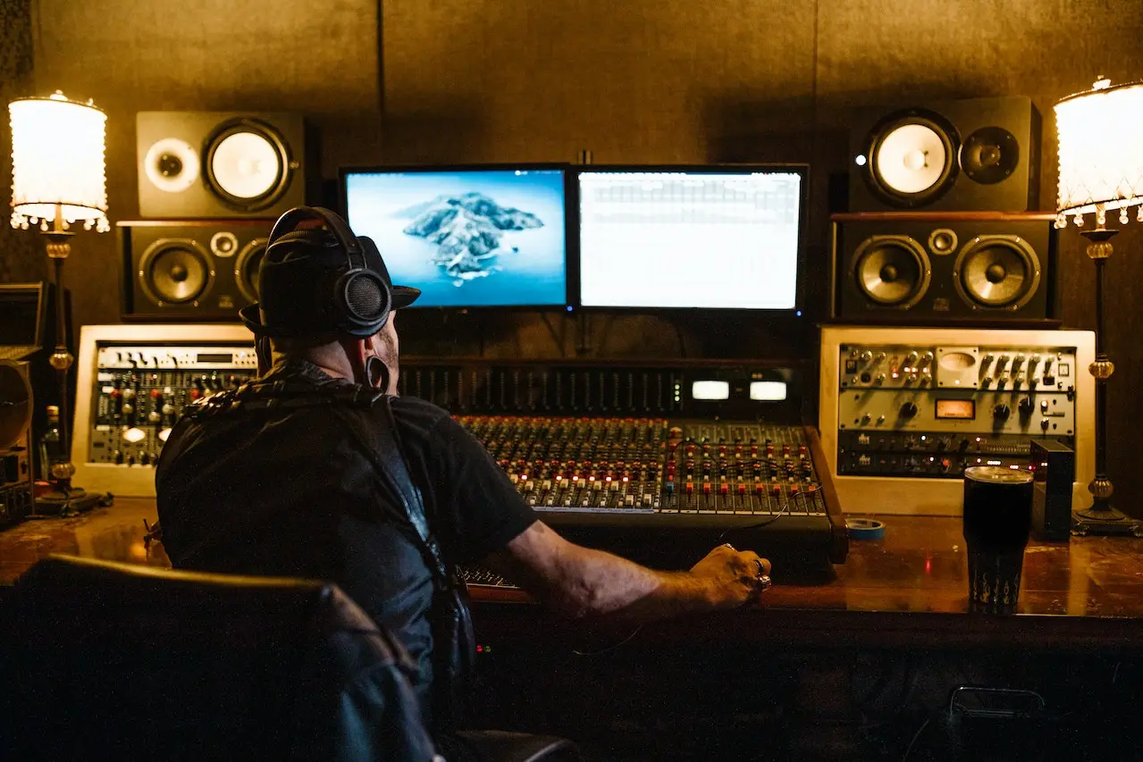 A man sitting at the mixing desk in front of two monitors.