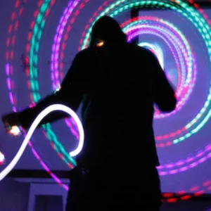 A person holding a light up stick in front of a neon spiral.