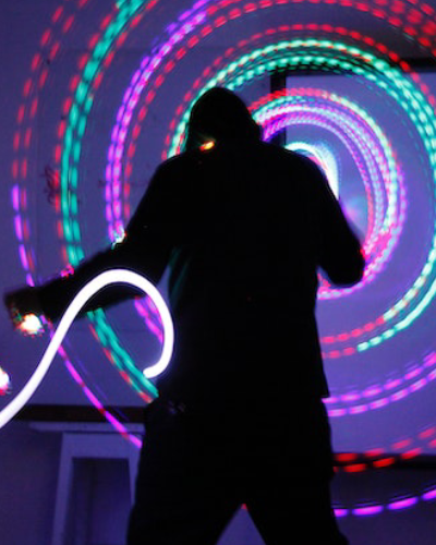 A person holding a light up stick in front of a neon spiral.