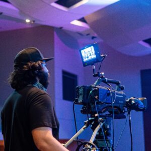 A man with a camera and microphone in front of a room.