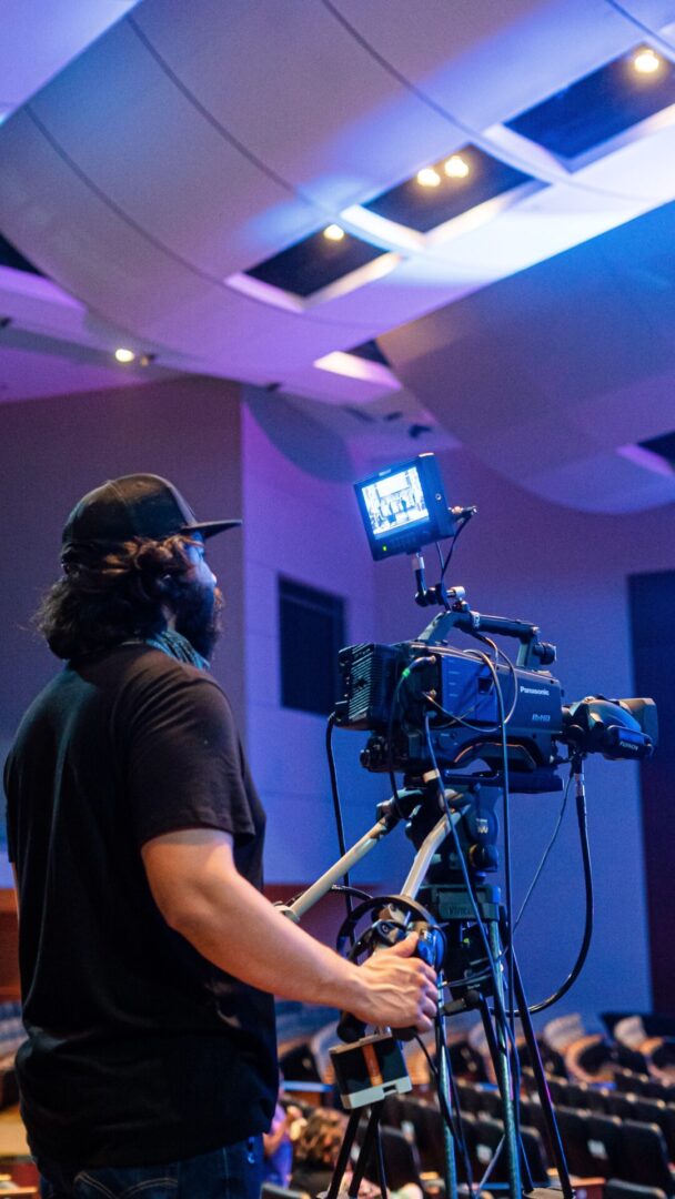 A man with a camera and microphone in front of a room.